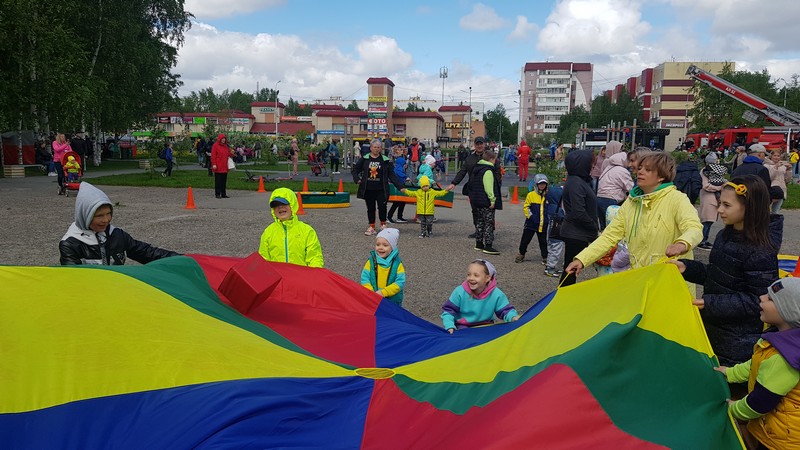на фотографии дети в сопровождении взрослых играют в «веселый парашют», в сквере у ДК «Строитель»